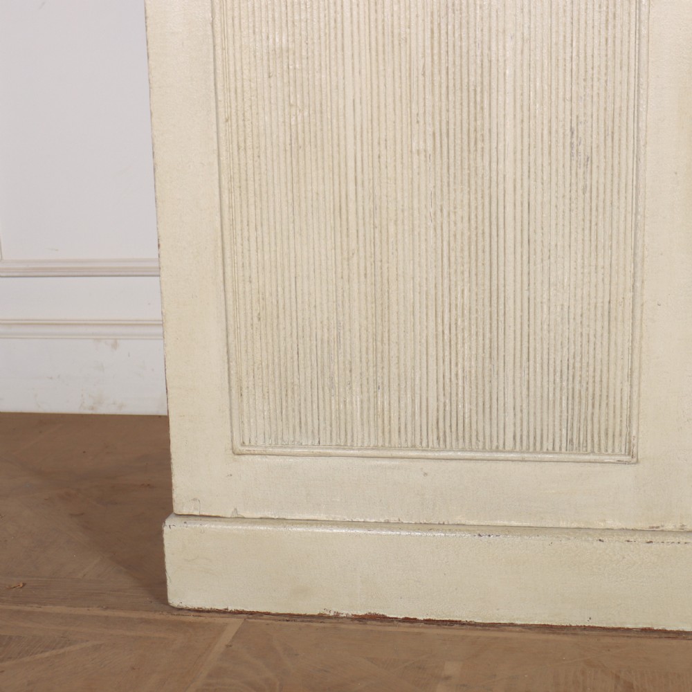 A Swedish style off-white painted wooden linen cupboard featuring three reeded panel doors with small brass knobs. View II