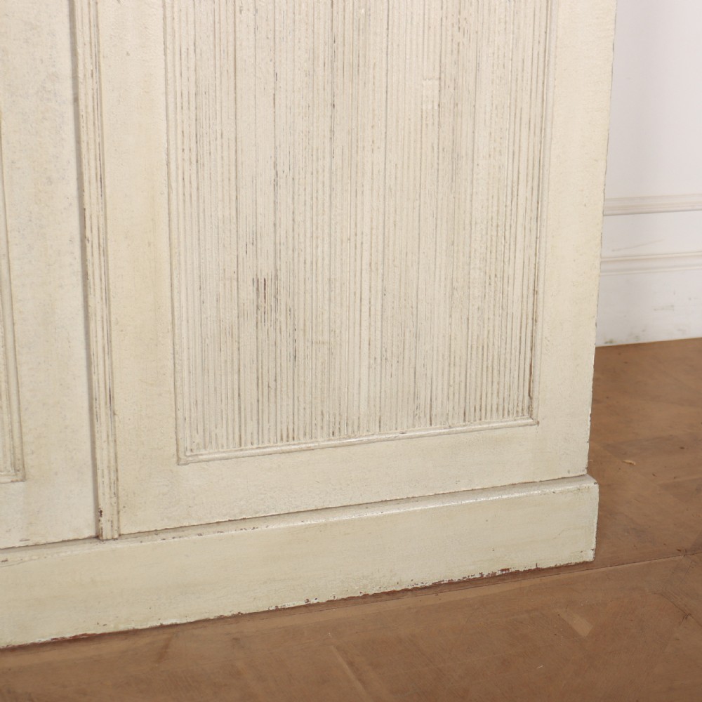 A Swedish style off-white painted wooden linen cupboard featuring three reeded panel doors with small brass knobs. View V