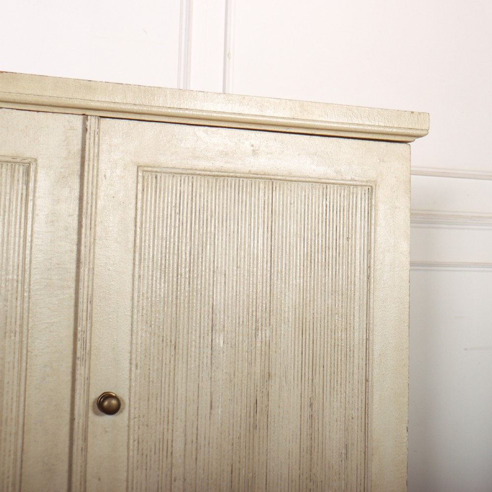 A Swedish style off-white painted wooden linen cupboard featuring three reeded panel doors with small brass knobs. View VI