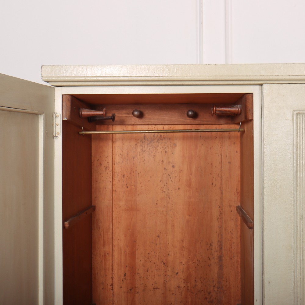 A Swedish style off-white painted wooden linen cupboard featuring three reeded panel doors with small brass knobs. View IX