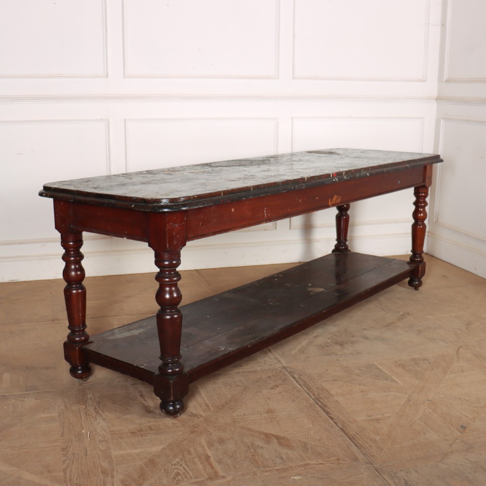 A long Victorian mahogany drapers table featuring turned legs and a low potboard shelf.