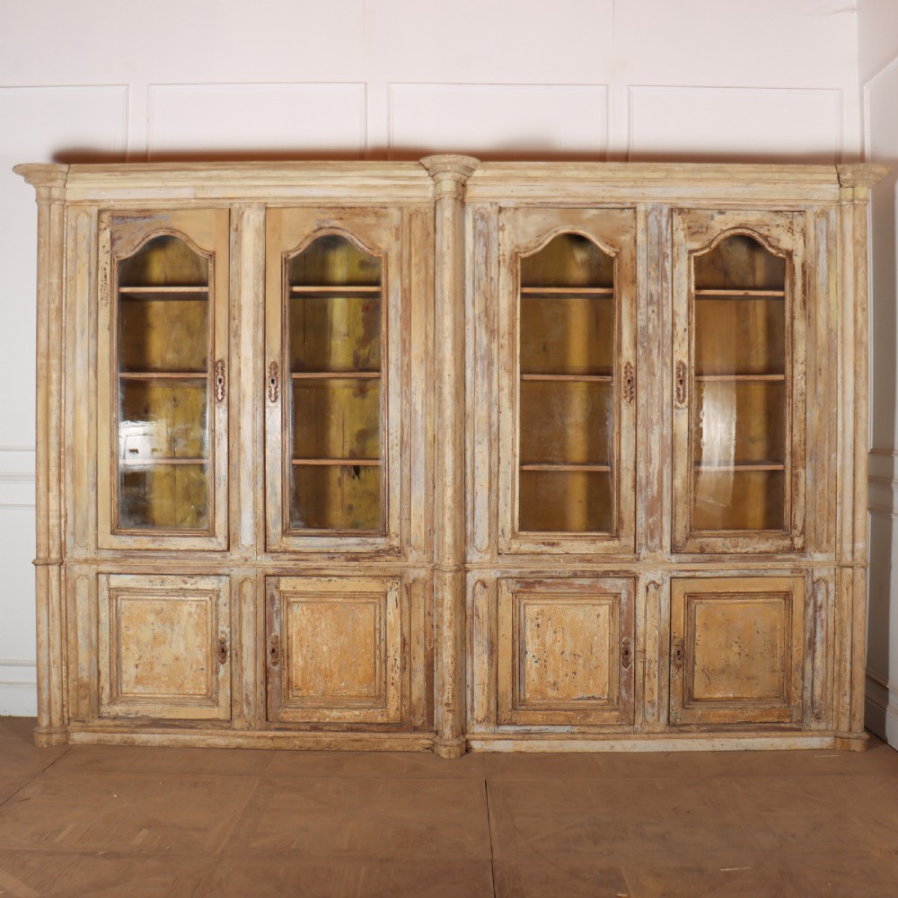 A large antique French library bookcase with four glazed upper doors, four panelled lower doors, and a distressed painted finish.