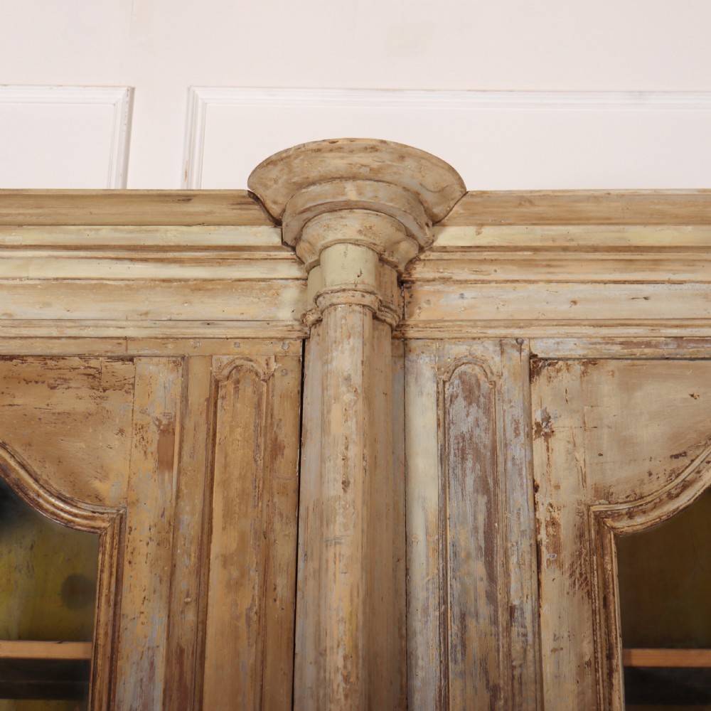 A large antique French library bookcase with four glazed upper doors, four panelled lower doors, and a distressed painted finish. View VII
