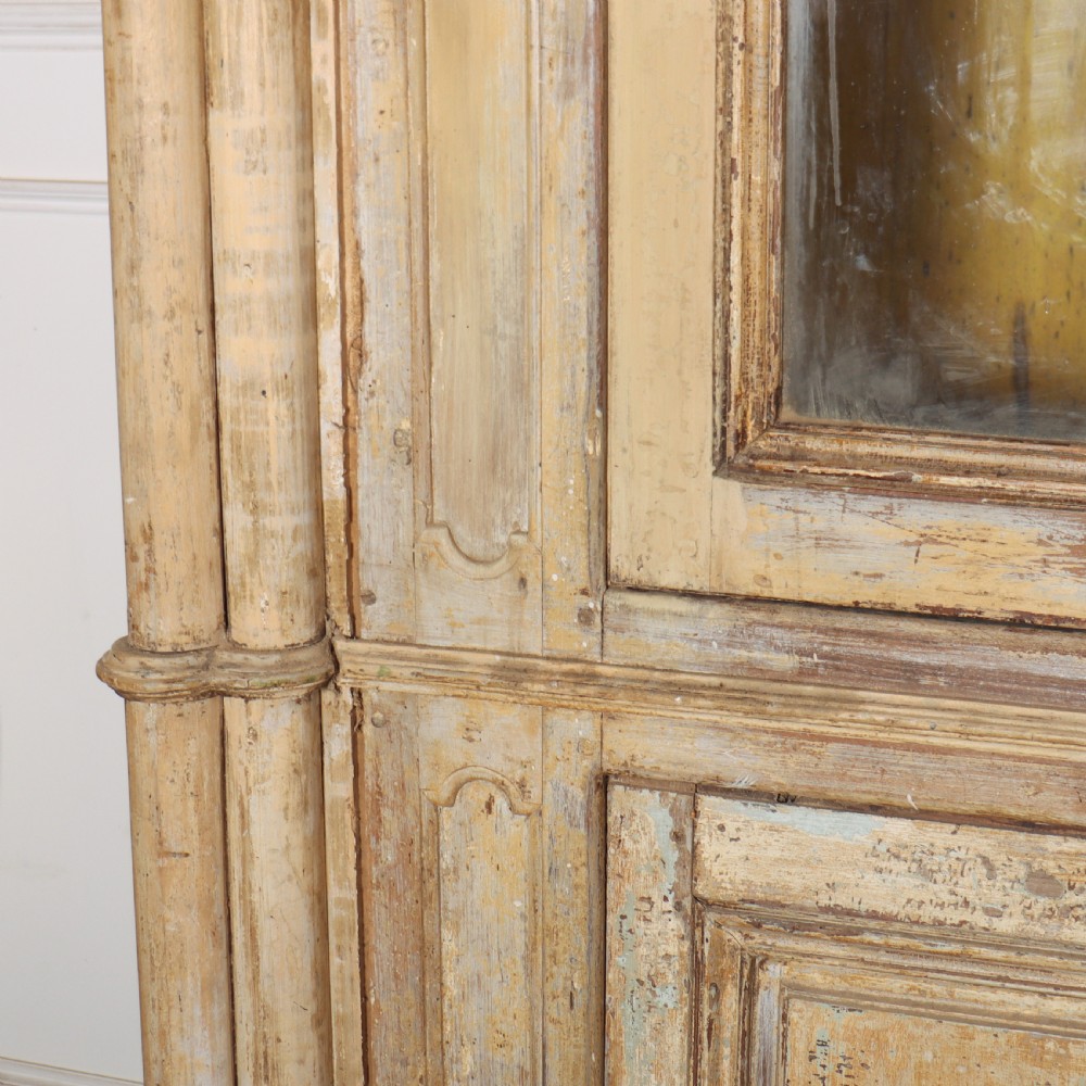 A large antique French library bookcase with four glazed upper doors, four panelled lower doors, and a distressed painted finish. View VIII