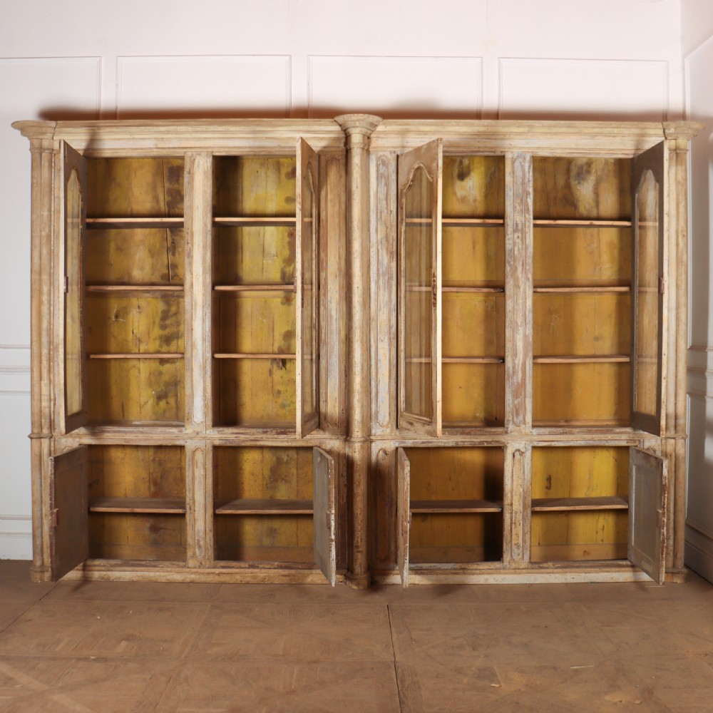 A large antique French library bookcase with four glazed upper doors, four panelled lower doors, and a distressed painted finish. View XIII