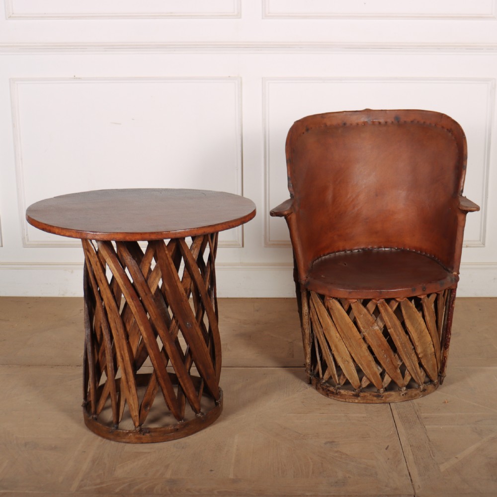 A rustic furniture set featuring a curved tub armchair and a matching round side table, both constructed with diagonally woven willow slat bases and tan leather tops.