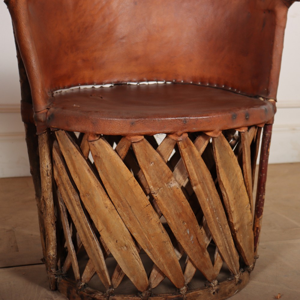 A rustic furniture set featuring a curved tub armchair and a matching round side table, both constructed with diagonally woven willow slat bases and tan leather tops. View VI