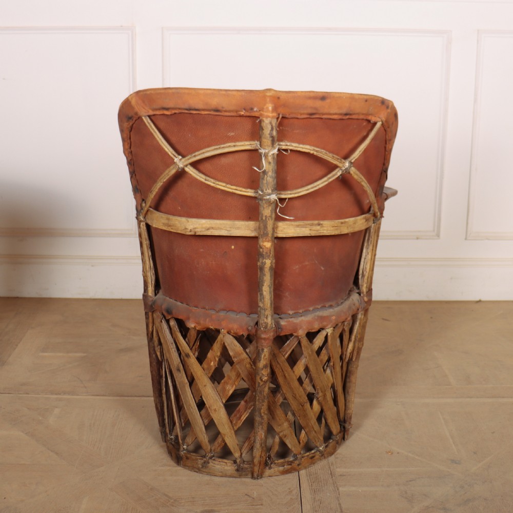 A rustic furniture set featuring a curved tub armchair and a matching round side table, both constructed with diagonally woven willow slat bases and tan leather tops. View IX