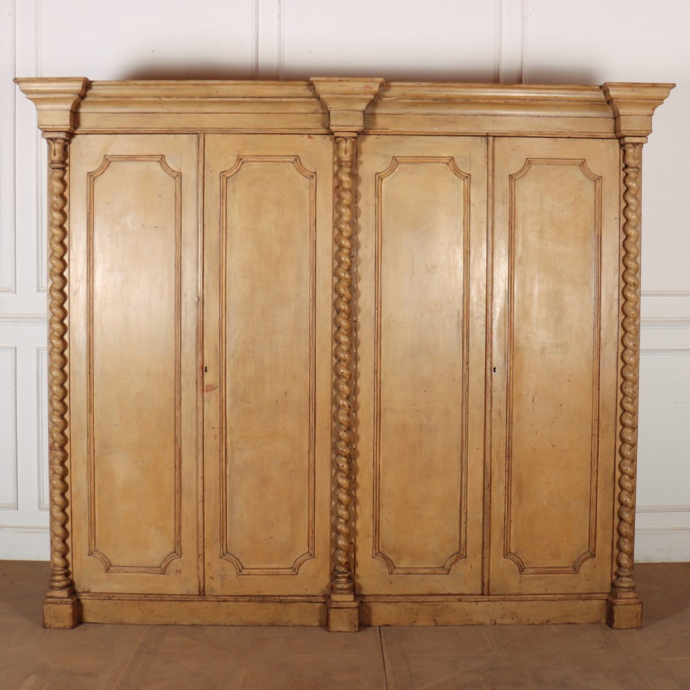 A large four-door cream painted wooden wardrobe featuring carved barley twist pilasters and shaped door panels.