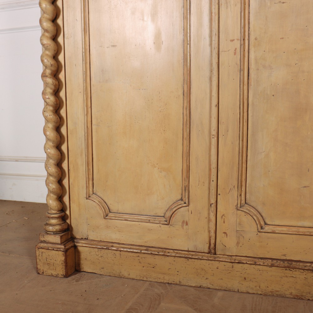 A large four-door cream painted wooden wardrobe featuring carved barley twist pilasters and shaped door panels. View VII