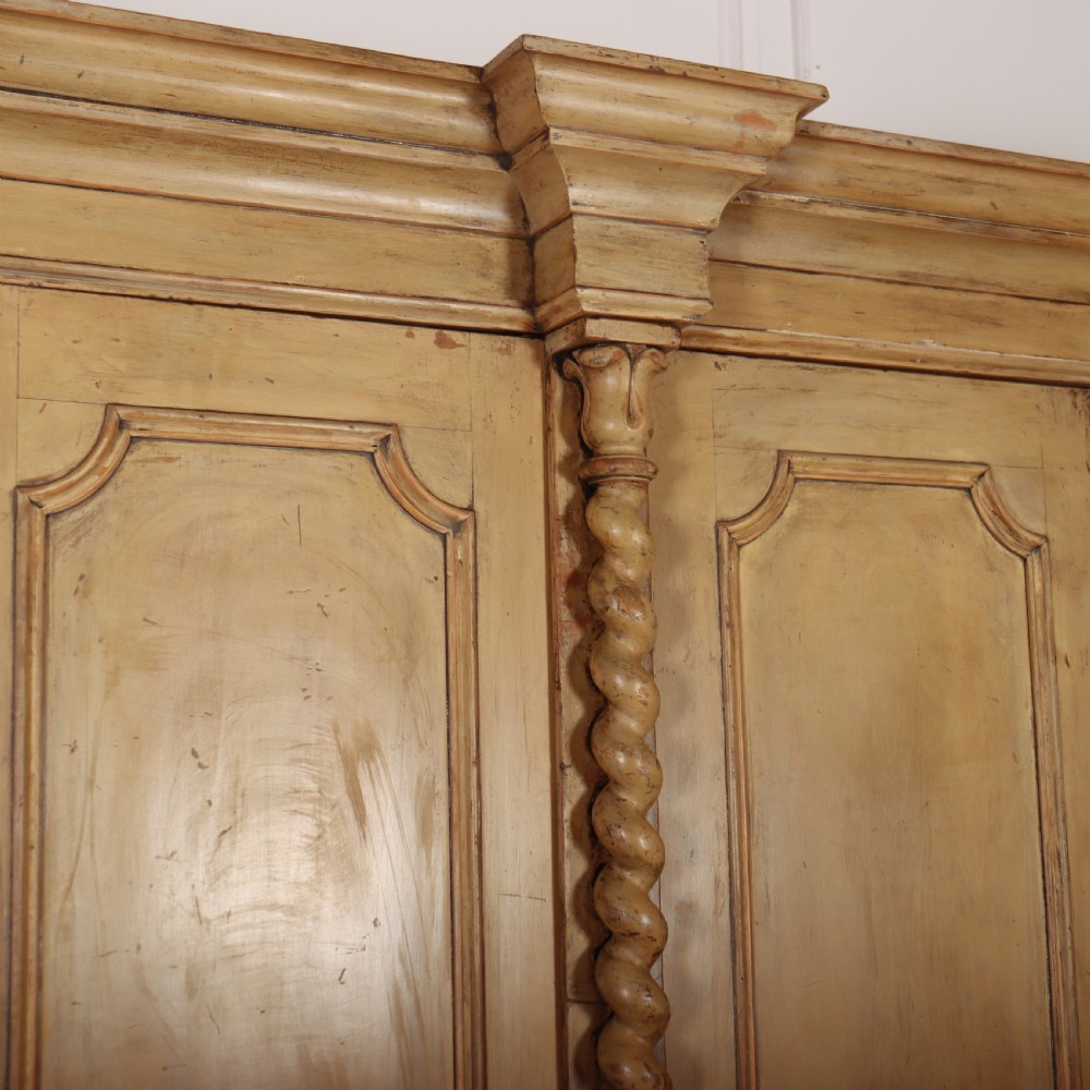 A large four-door cream painted wooden wardrobe featuring carved barley twist pilasters and shaped door panels. View IX
