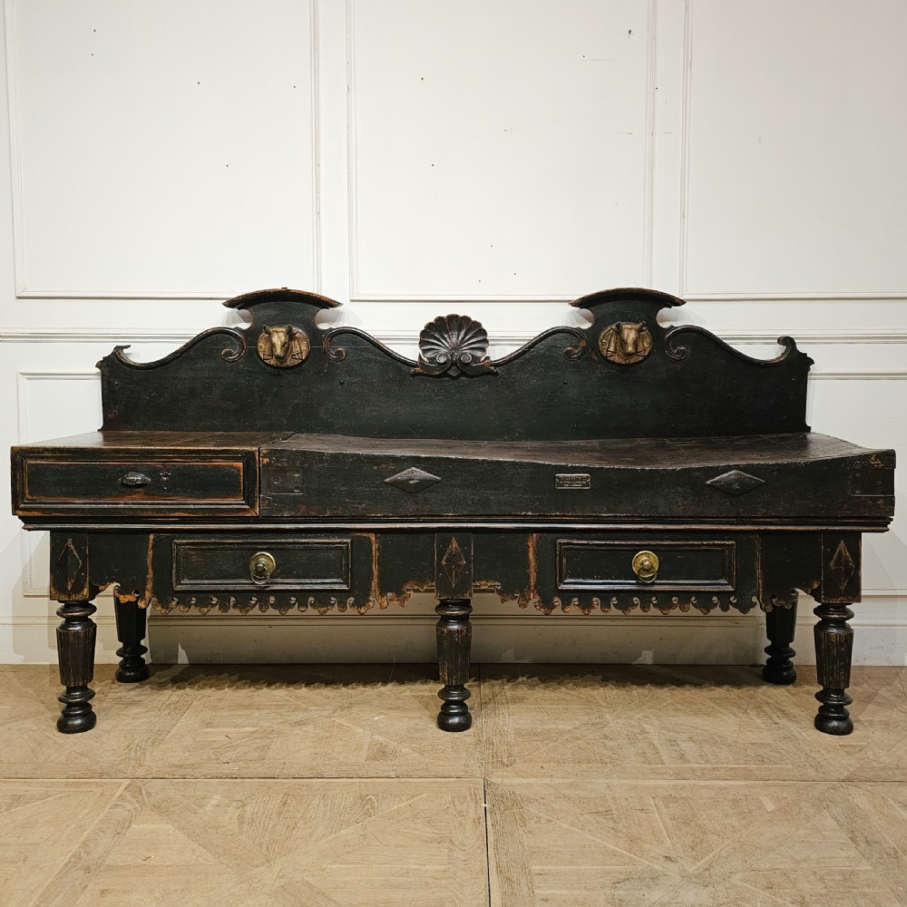 A 19th-century French ebonised timber butchers block featuring a carved splashback with brass bull head mounts, turned legs, and lower drawers.