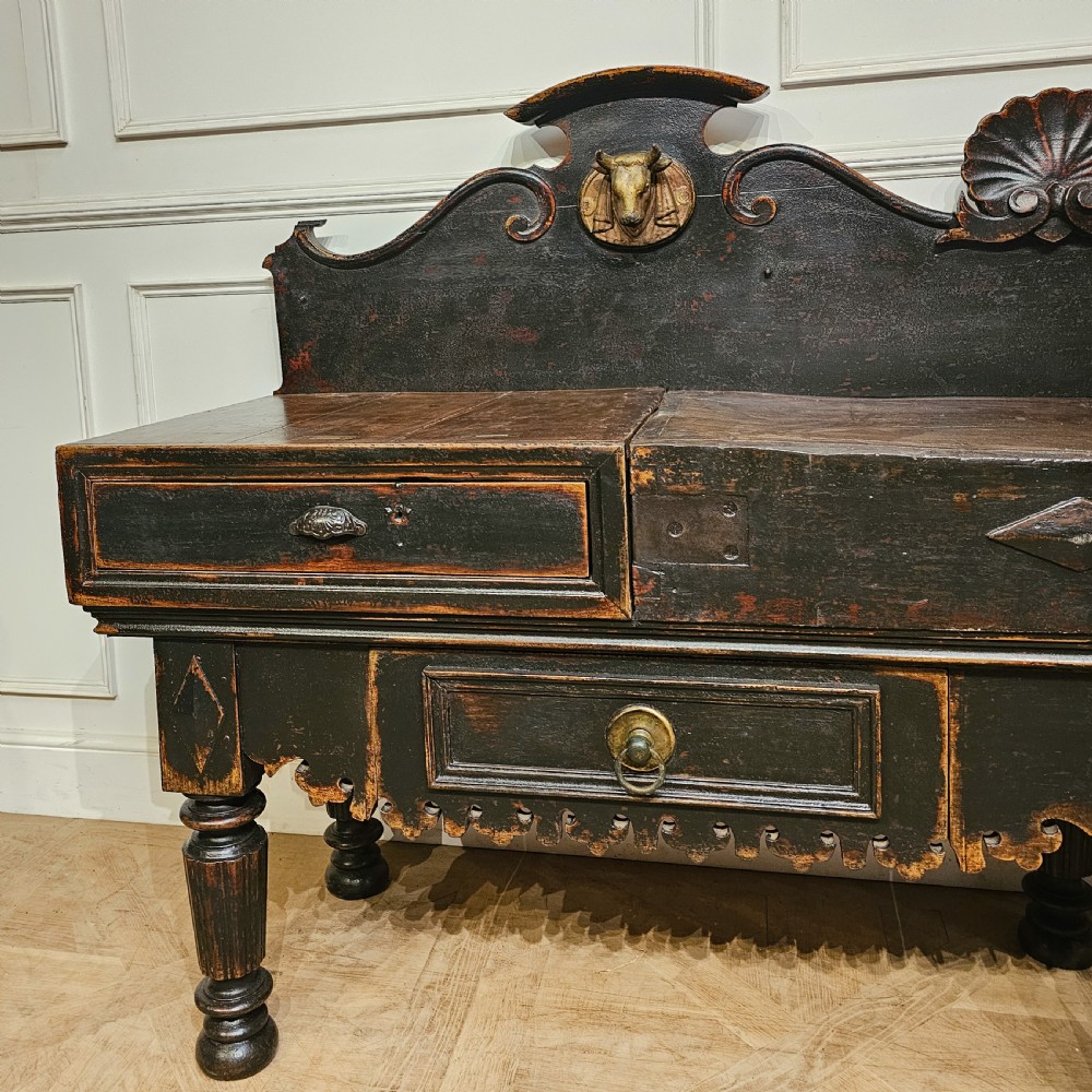 A 19th-century French ebonised timber butchers block featuring a carved splashback with brass bull head mounts, turned legs, and lower drawers. View II