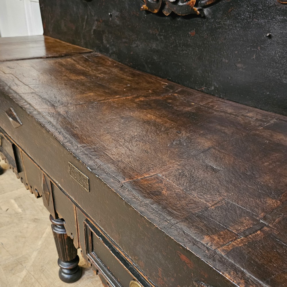 A 19th-century French ebonised timber butchers block featuring a carved splashback with brass bull head mounts, turned legs, and lower drawers. View V