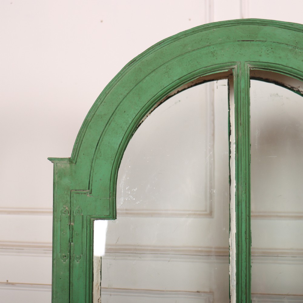 A 19th-century green painted display cabinet featuring twin arched glazed doors, a scalloped apron, and six turned legs joined by a shaped stretcher. View II
