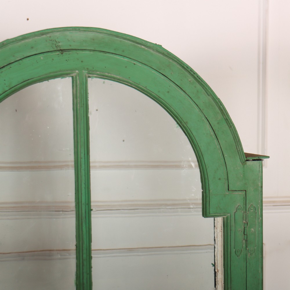 A 19th-century green painted display cabinet featuring twin arched glazed doors, a scalloped apron, and six turned legs joined by a shaped stretcher. View IV
