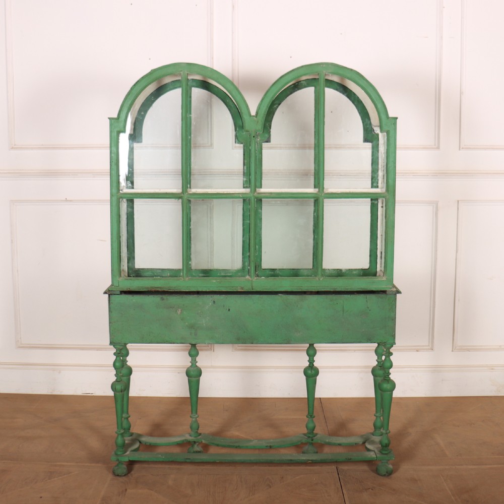 A 19th-century green painted display cabinet featuring twin arched glazed doors, a scalloped apron, and six turned legs joined by a shaped stretcher. View IX