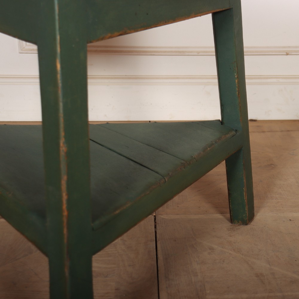 A circular wooden cricket table featuring an unpainted pale timber top mounted on a dark green painted three-legged base with a lower triangular shelf. View III