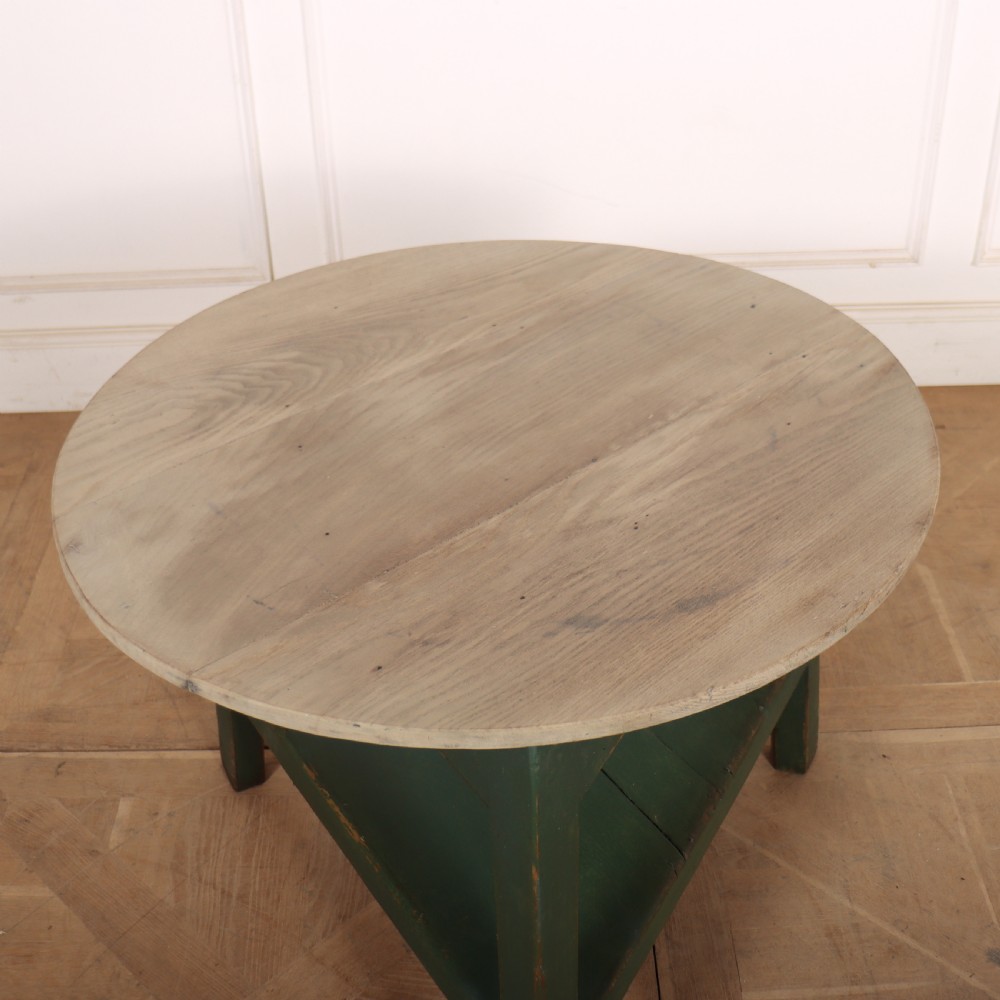 A circular wooden cricket table featuring an unpainted pale timber top mounted on a dark green painted three-legged base with a lower triangular shelf. View V