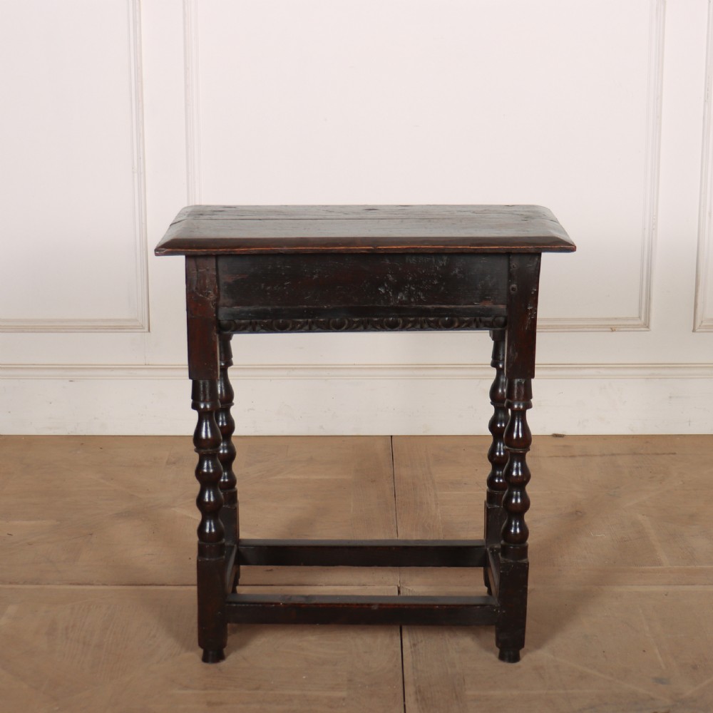 An 18th-century dark oak side table featuring turned legs, lower box stretchers, and a carved apron frieze.