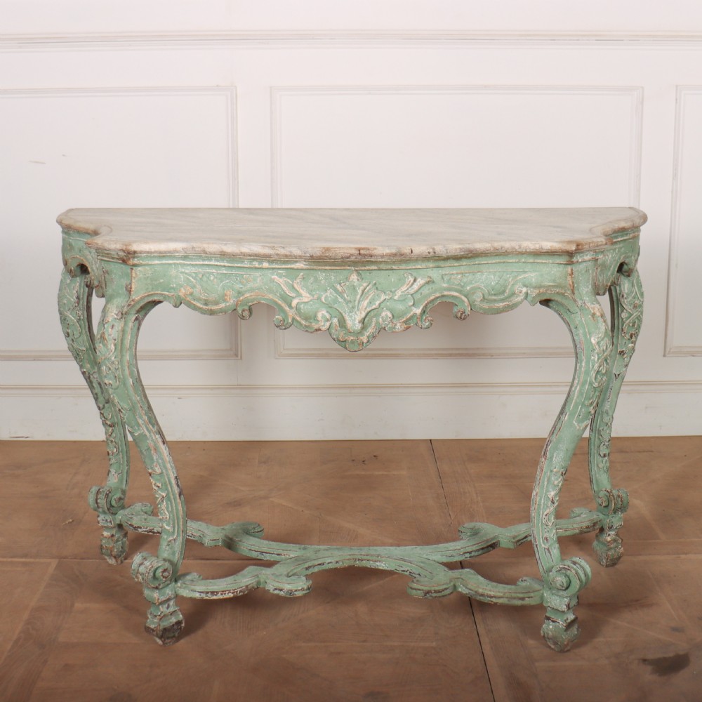An Italian Rococo style console table featuring a distressed pale green painted finish, a serpentine marble top, intricate scroll carvings, and a contoured X-form stretcher.