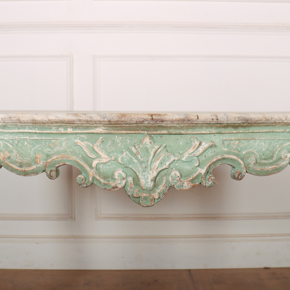 An Italian Rococo style console table featuring a distressed pale green painted finish, a serpentine marble top, intricate scroll carvings, and a contoured X-form stretcher. View II