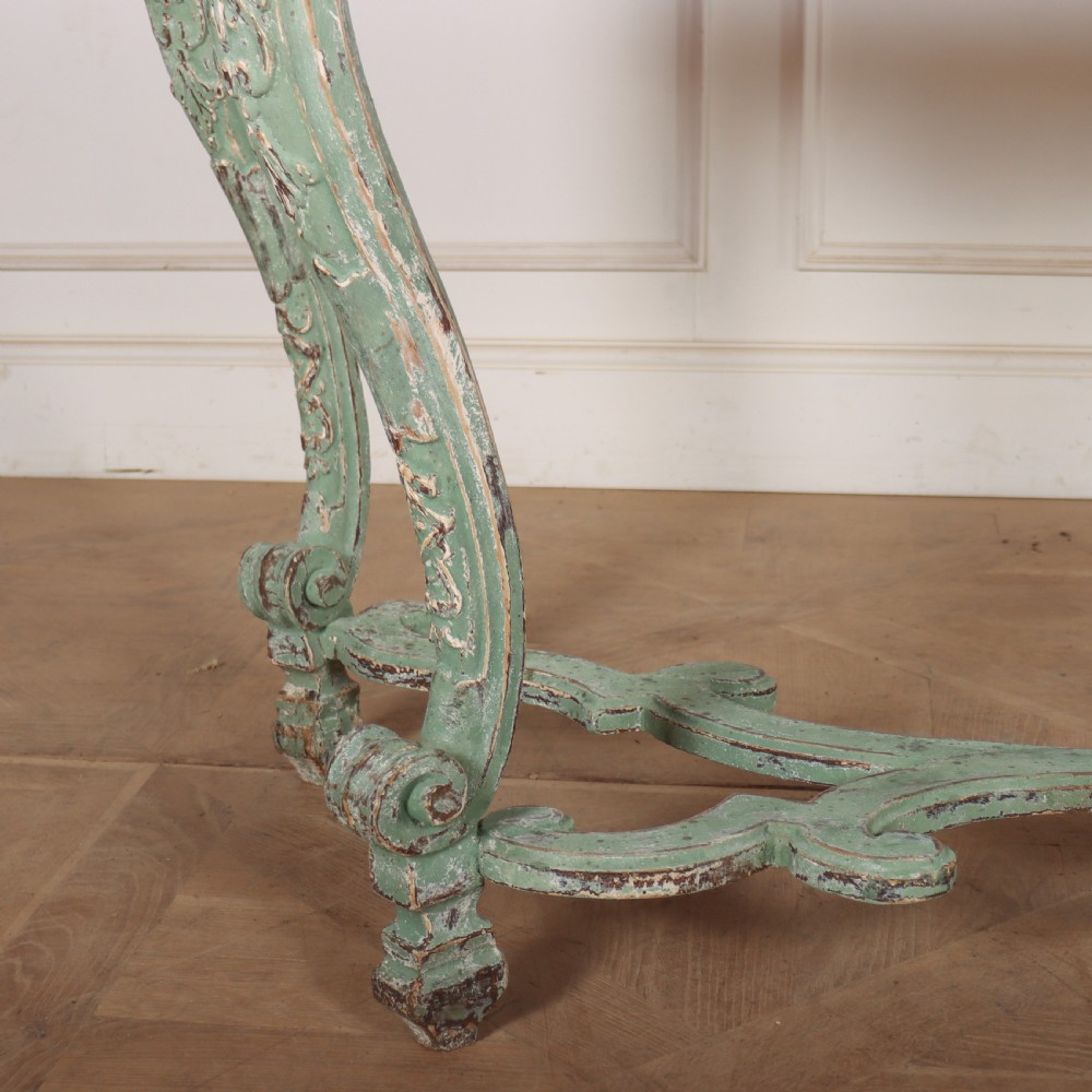 An Italian Rococo style console table featuring a distressed pale green painted finish, a serpentine marble top, intricate scroll carvings, and a contoured X-form stretcher. View III