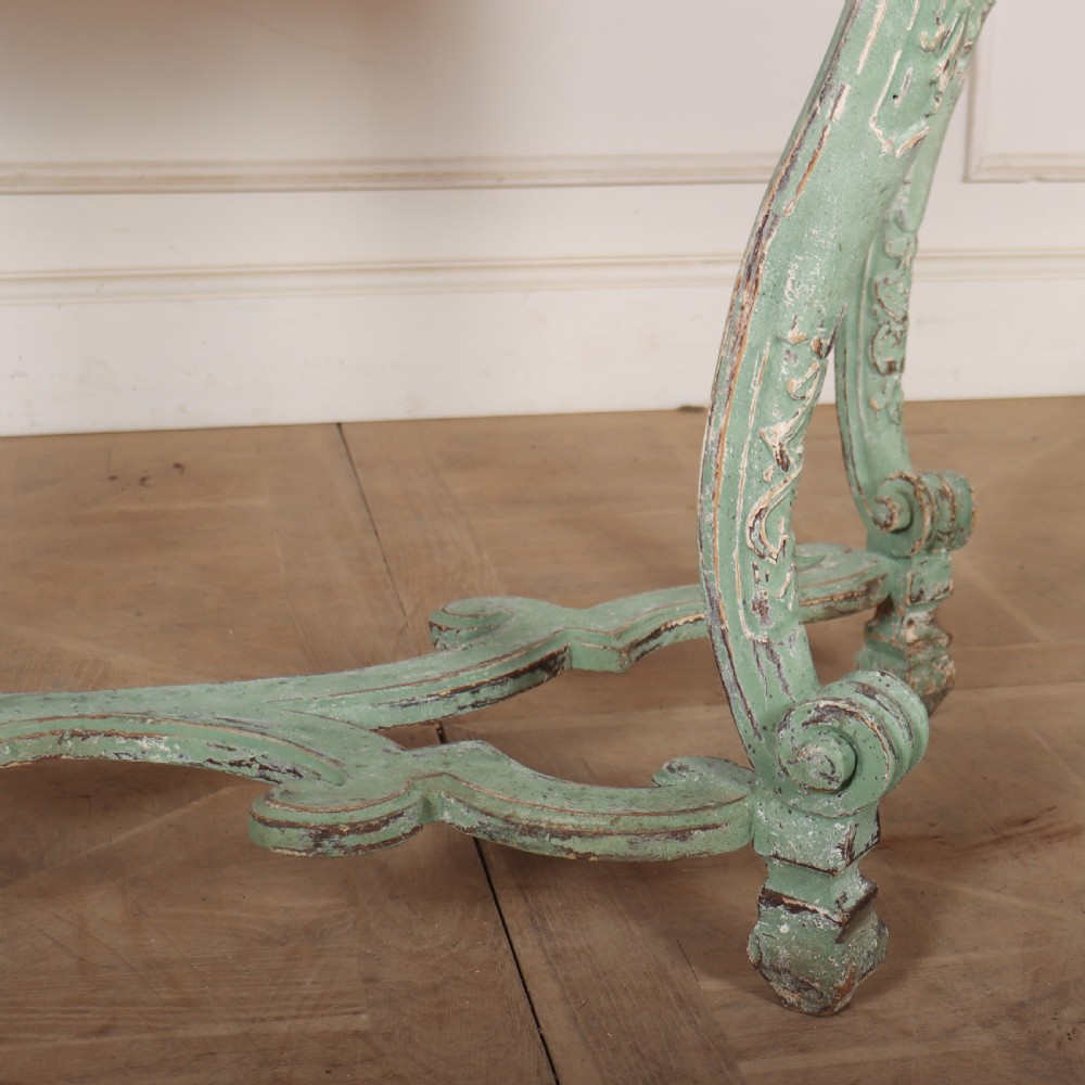 An Italian Rococo style console table featuring a distressed pale green painted finish, a serpentine marble top, intricate scroll carvings, and a contoured X-form stretcher. View IV