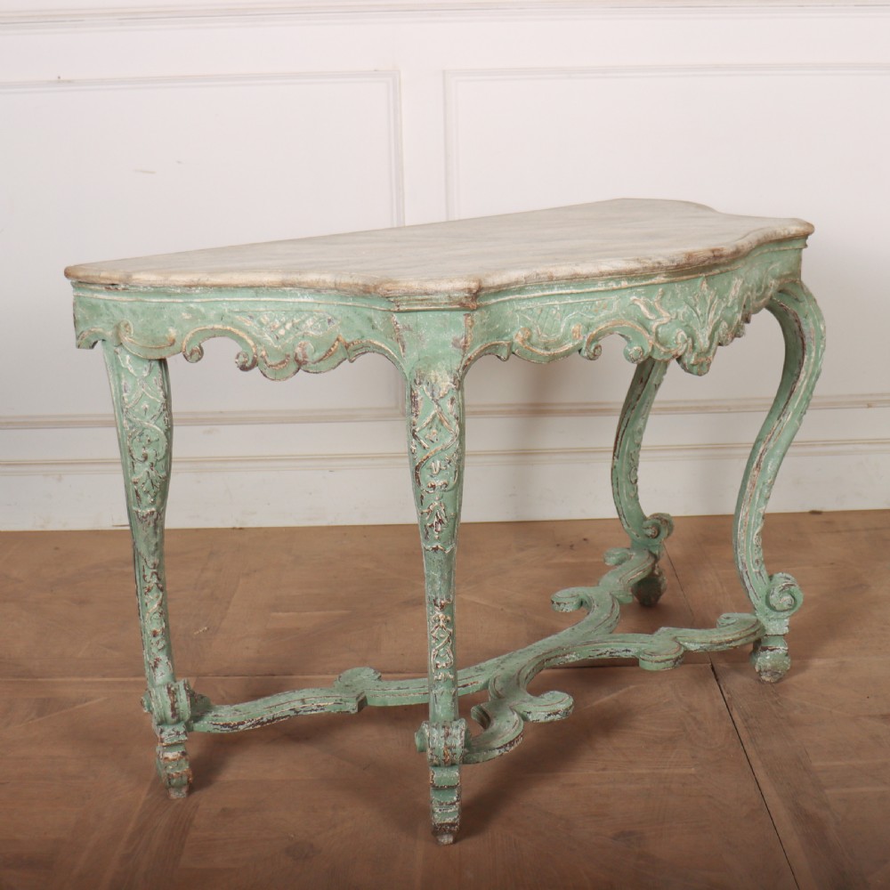 An Italian Rococo style console table featuring a distressed pale green painted finish, a serpentine marble top, intricate scroll carvings, and a contoured X-form stretcher. View V