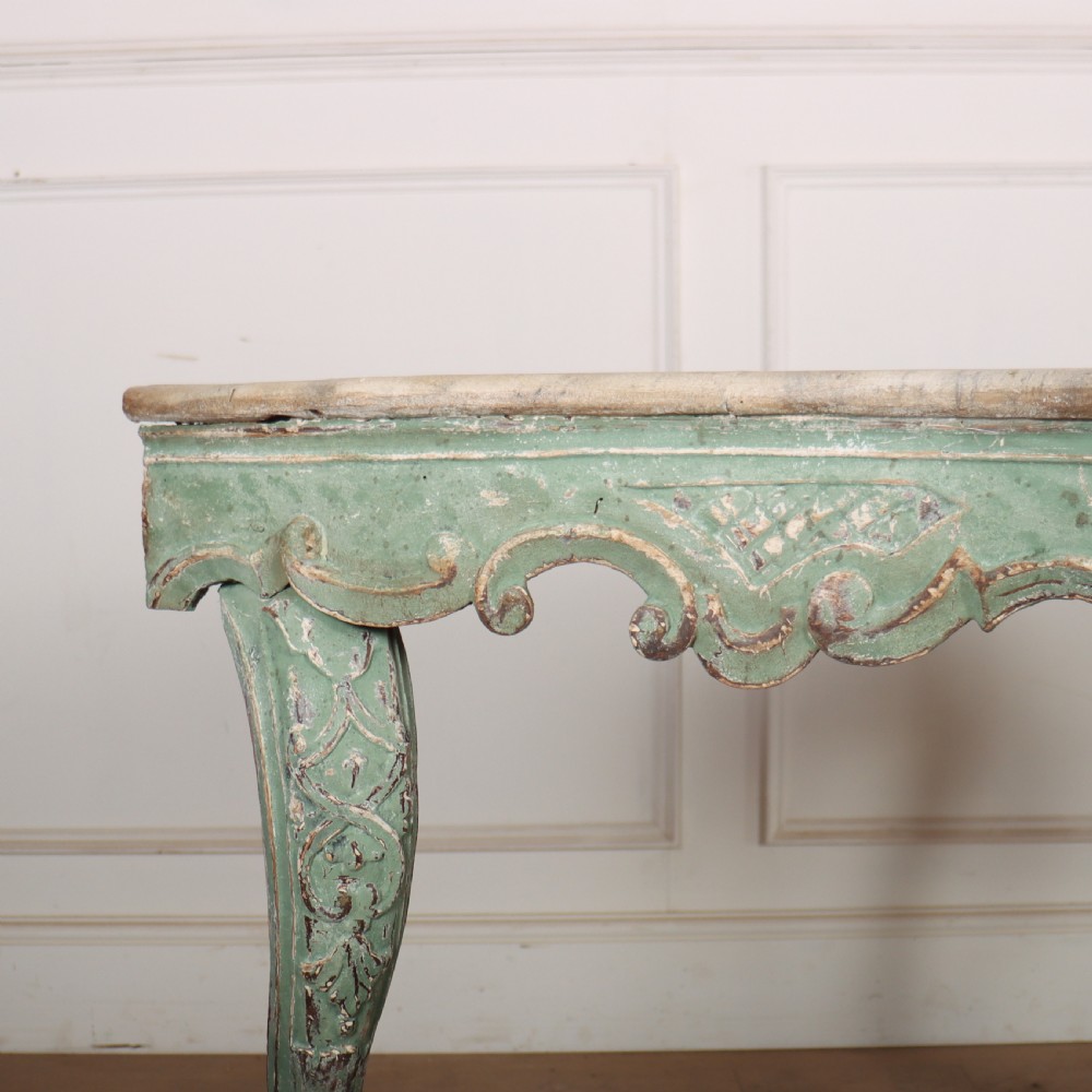 An Italian Rococo style console table featuring a distressed pale green painted finish, a serpentine marble top, intricate scroll carvings, and a contoured X-form stretcher. View VI