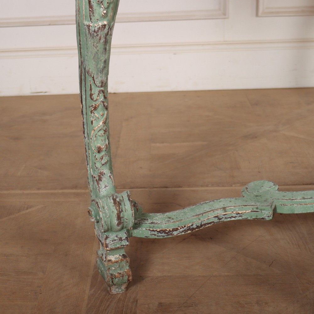 An Italian Rococo style console table featuring a distressed pale green painted finish, a serpentine marble top, intricate scroll carvings, and a contoured X-form stretcher. View VII