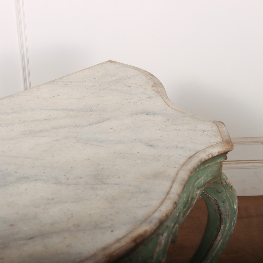 An Italian Rococo style console table featuring a distressed pale green painted finish, a serpentine marble top, intricate scroll carvings, and a contoured X-form stretcher. View IX