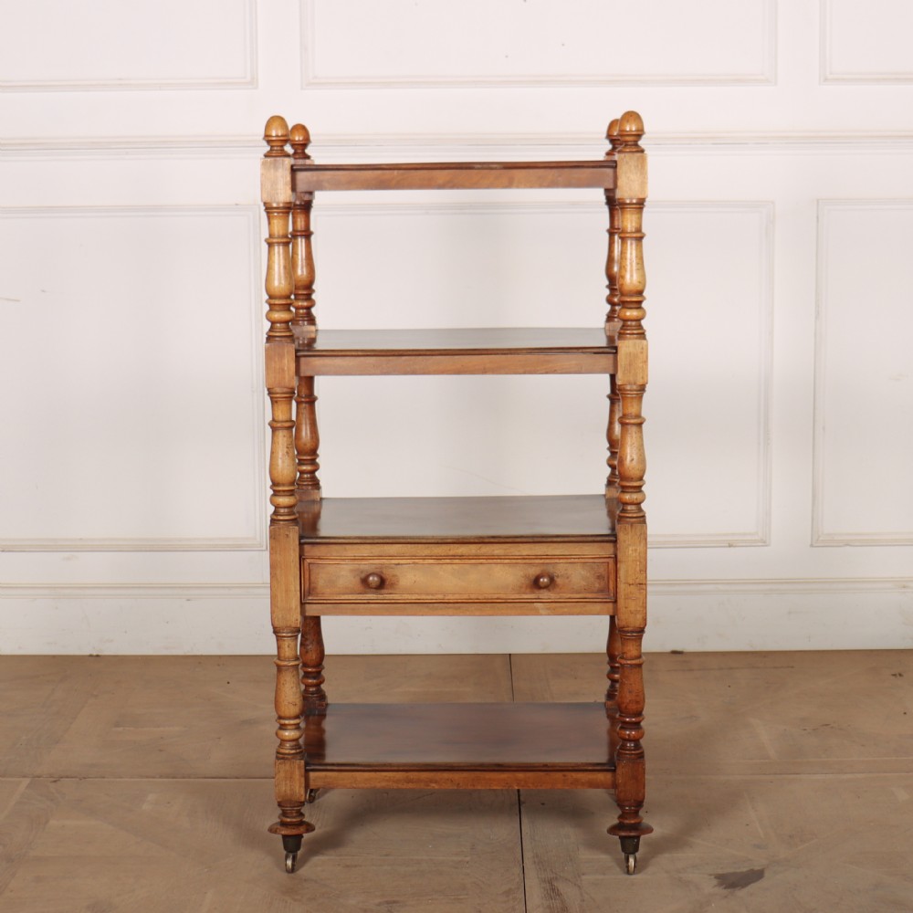 A 19th-century English four-tier wooden whatnot featuring turned support columns, a single drawer, top finials, and brass castors.