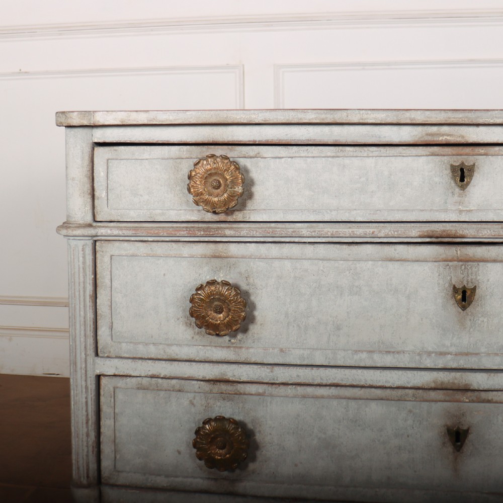 A Louis XVI style pale grey painted oak commode featuring three drawers with gilded rosette handles and fluted legs. View II
