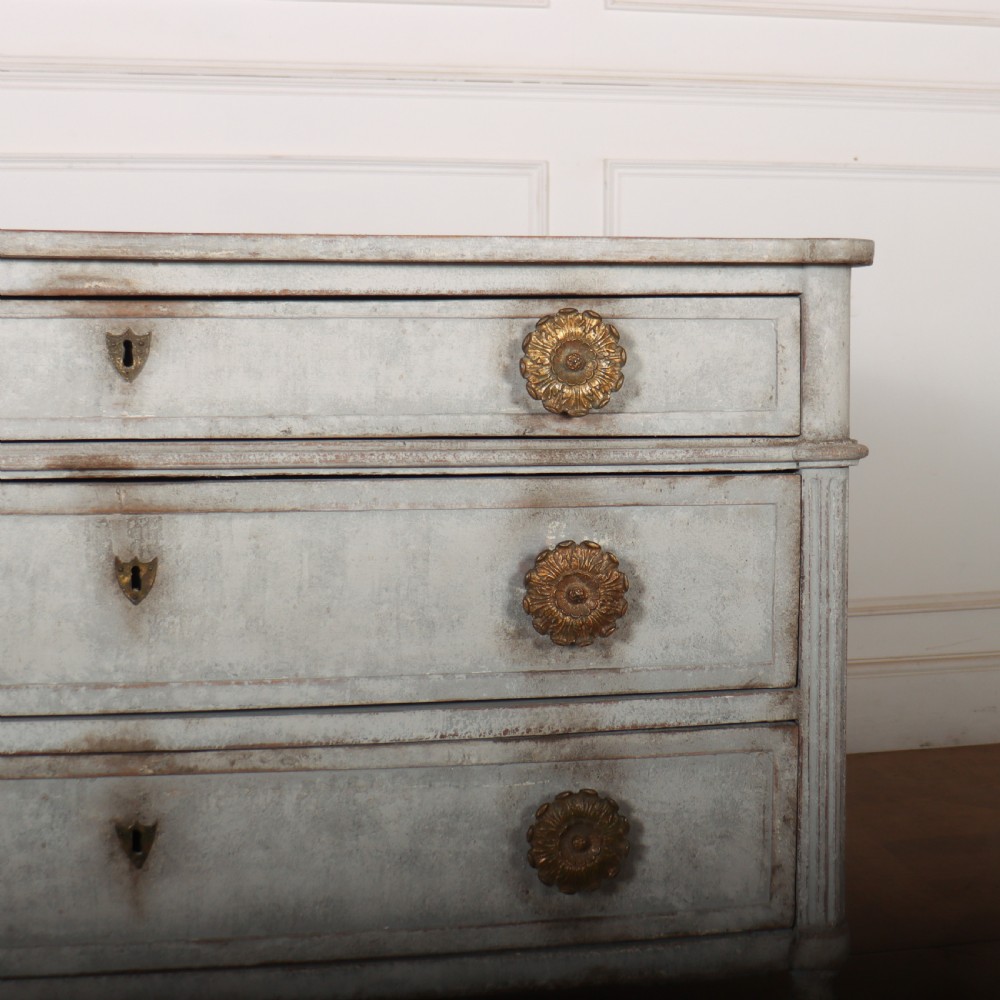 A Louis XVI style pale grey painted oak commode featuring three drawers with gilded rosette handles and fluted legs. View V