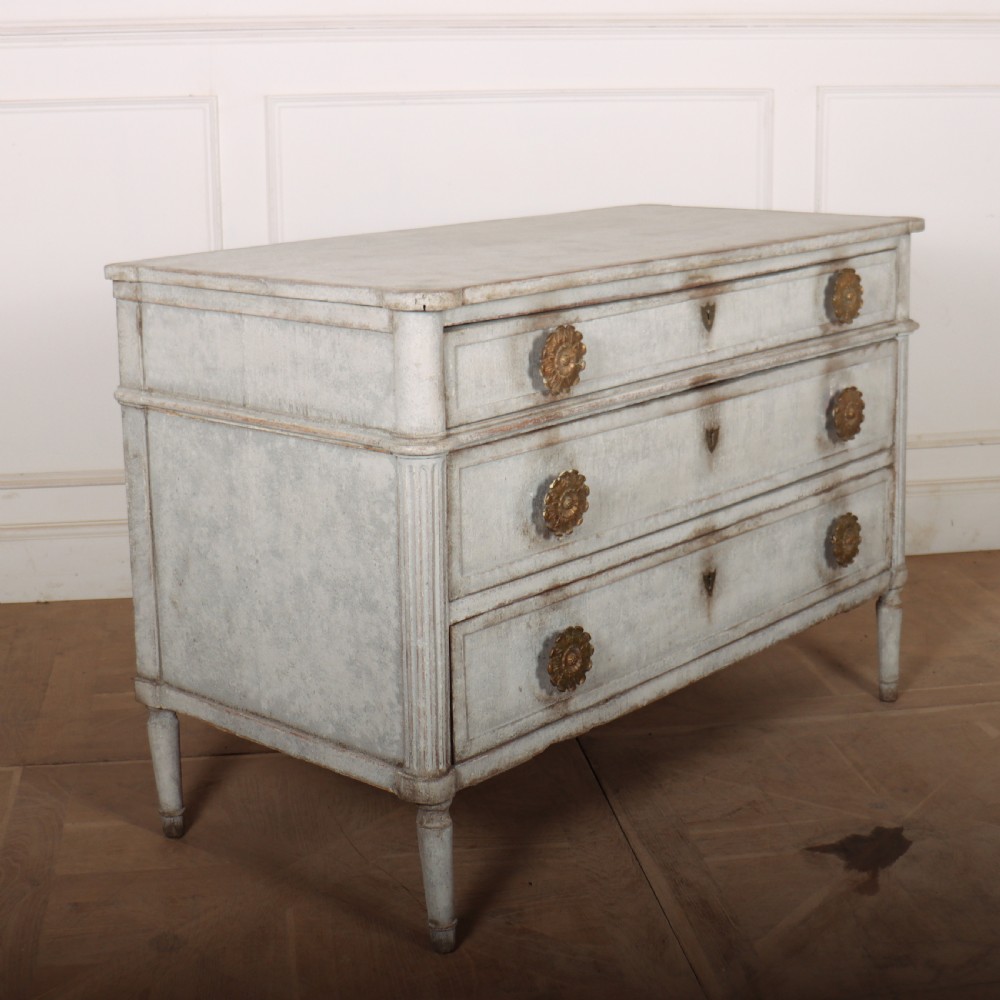 A Louis XVI style pale grey painted oak commode featuring three drawers with gilded rosette handles and fluted legs. View VIII