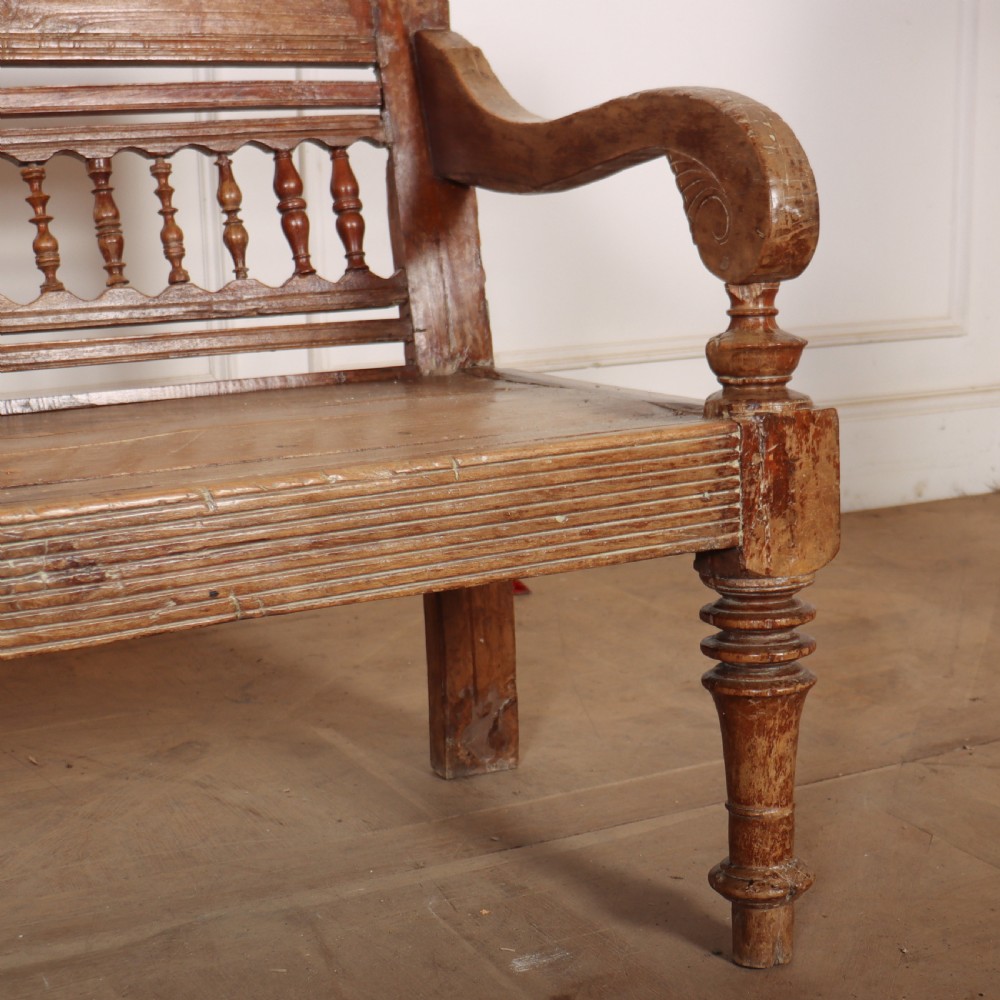A 19th-century bleached chestnut wooden settle featuring a spindle-detailed backrest, curved armrests, and turned front legs. View VII