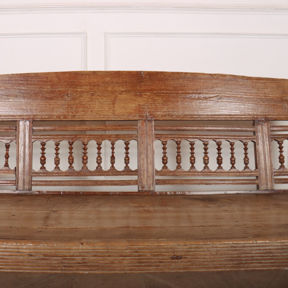 A 19th-century bleached chestnut wooden settle featuring a spindle-detailed backrest, curved armrests, and turned front legs. View V