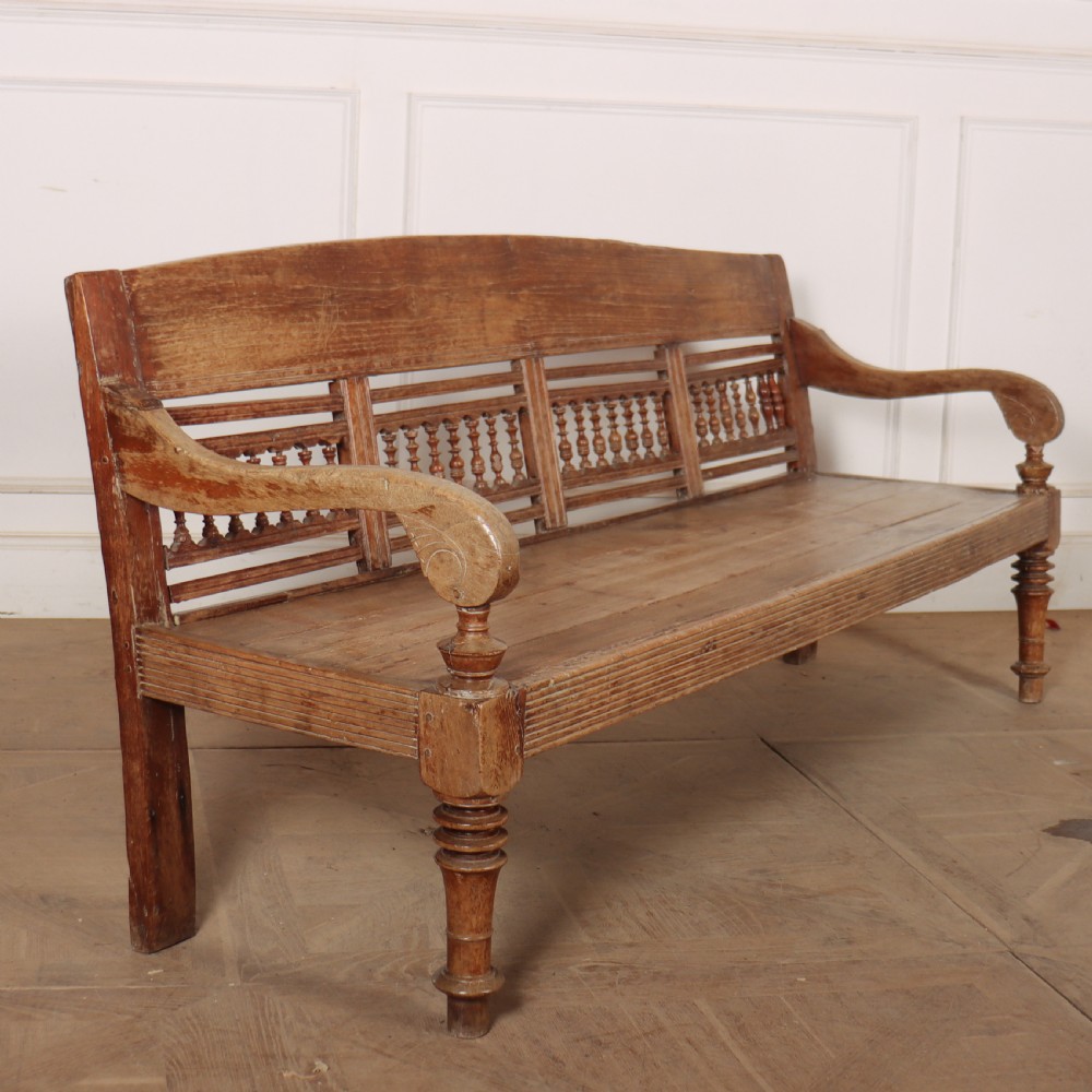 A 19th-century bleached chestnut wooden settle featuring a spindle-detailed backrest, curved armrests, and turned front legs.