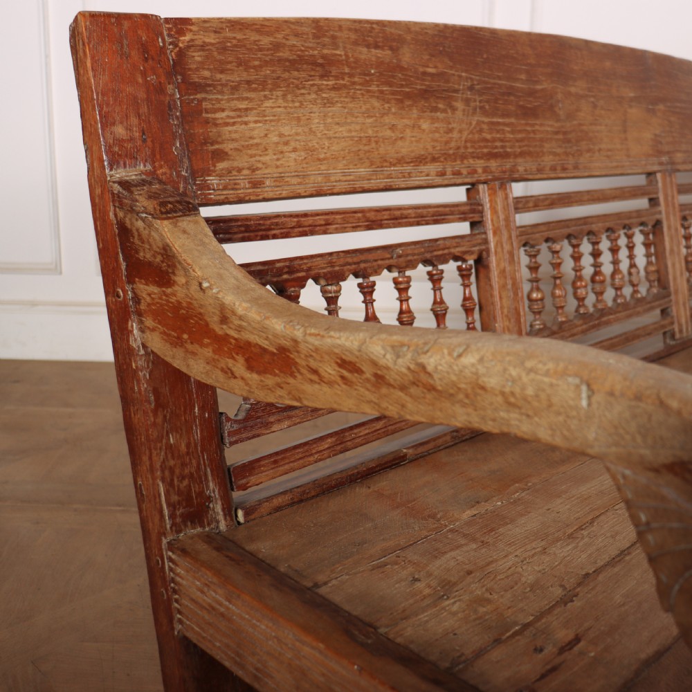 A 19th-century bleached chestnut wooden settle featuring a spindle-detailed backrest, curved armrests, and turned front legs. View VIII