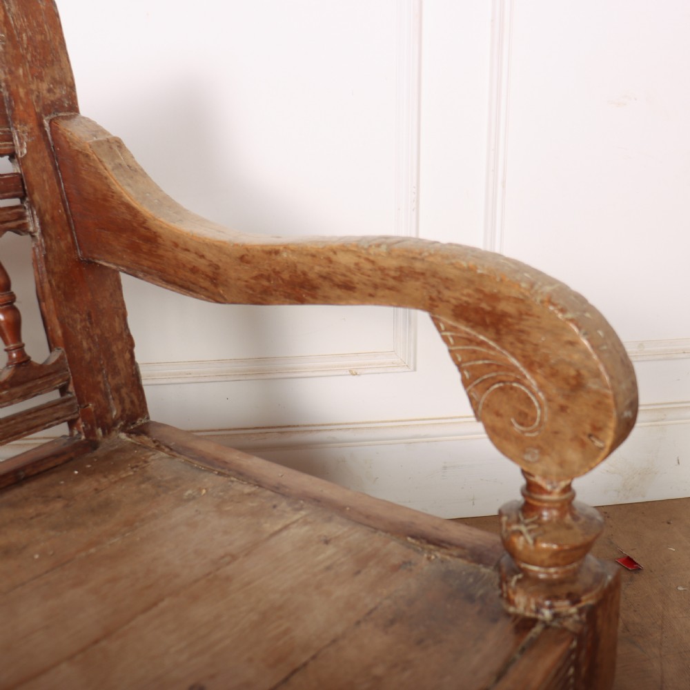 A 19th-century bleached chestnut wooden settle featuring a spindle-detailed backrest, curved armrests, and turned front legs. View X