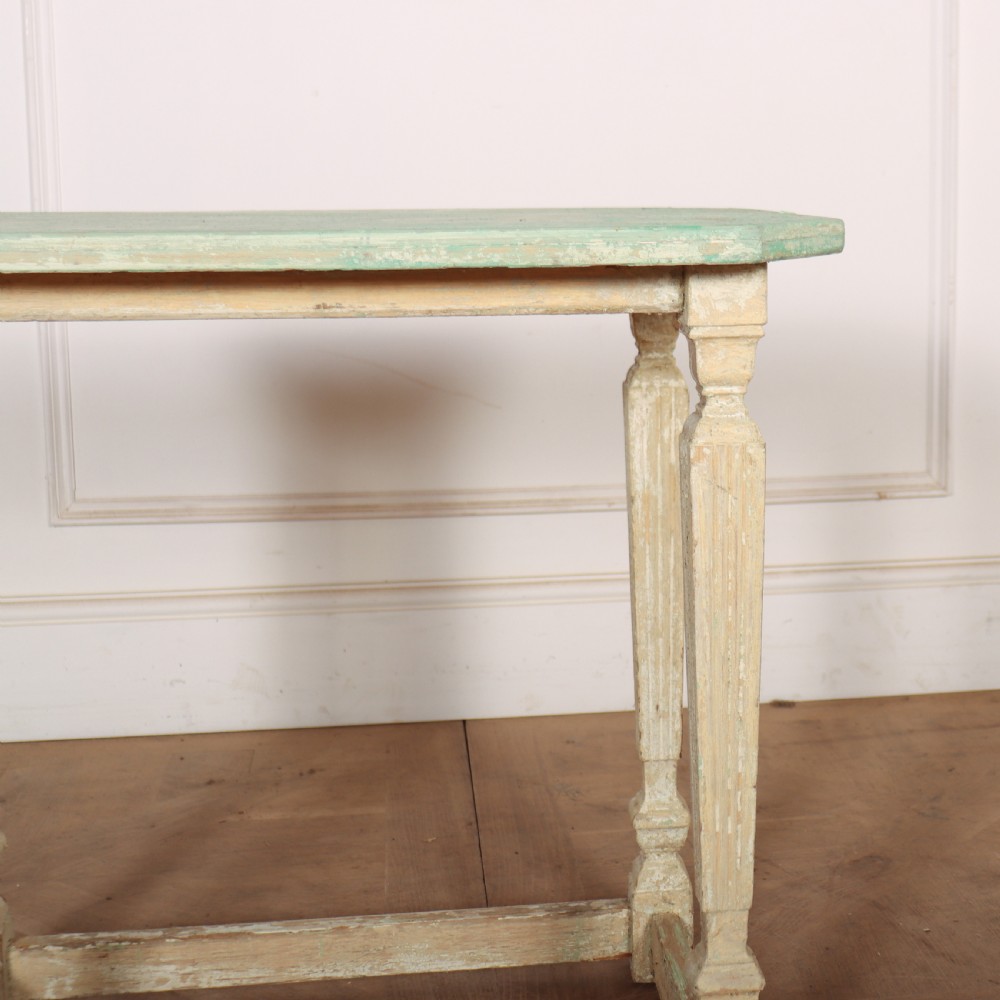 A small rectangular French wooden table with a pale green top, clipped corners, and cream distressed painted turned legs with a lower box stretcher. View VI