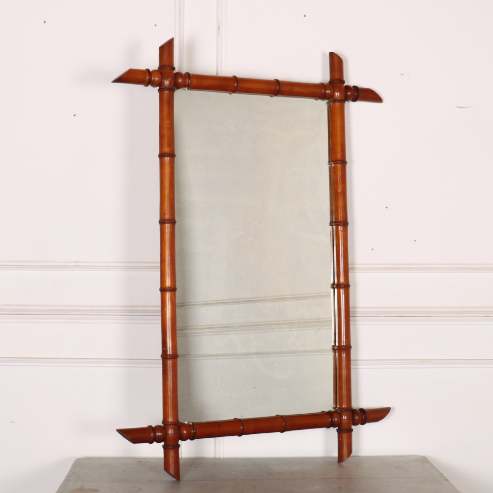 A rectangular wall mirror with a warm brown carved wood frame designed to simulate natural bamboo with crossed corner joints.