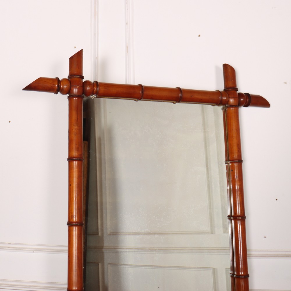 A rectangular wall mirror with a warm brown carved wood frame designed to simulate natural bamboo with crossed corner joints. View II