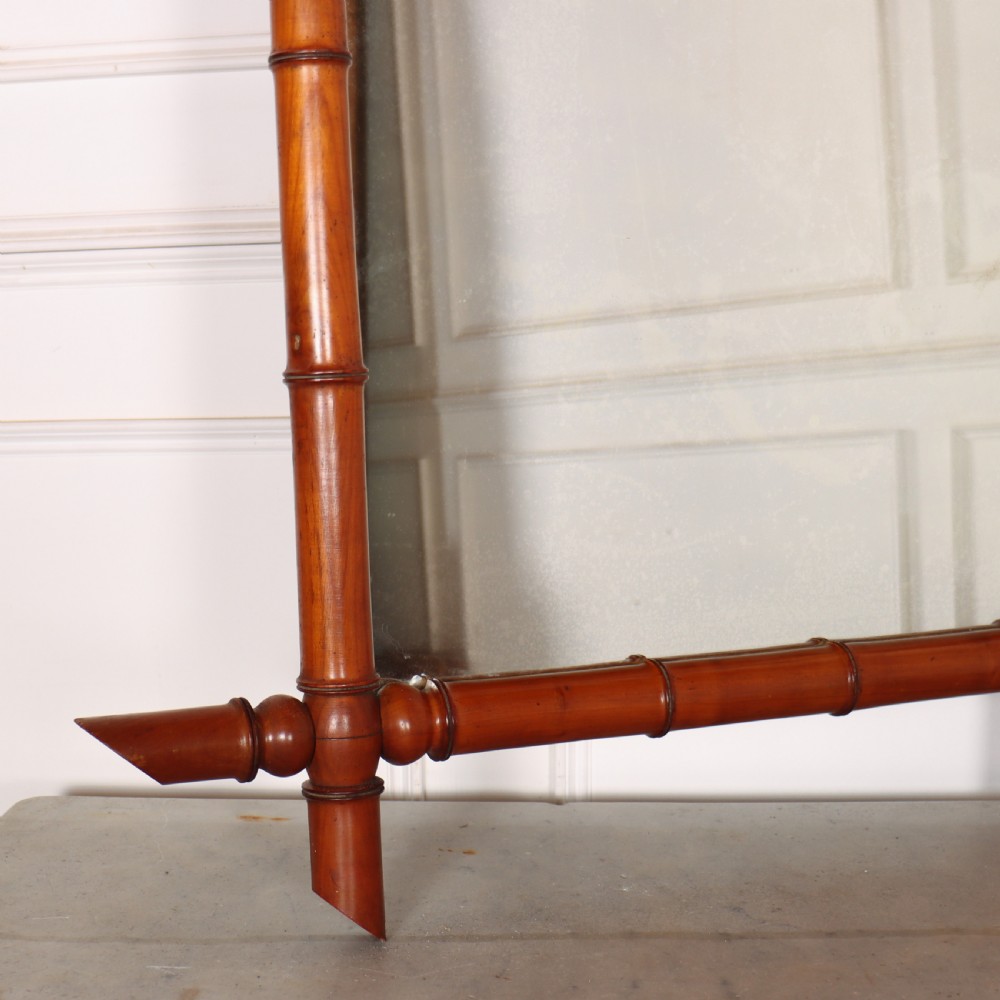A rectangular wall mirror with a warm brown carved wood frame designed to simulate natural bamboo with crossed corner joints. View III