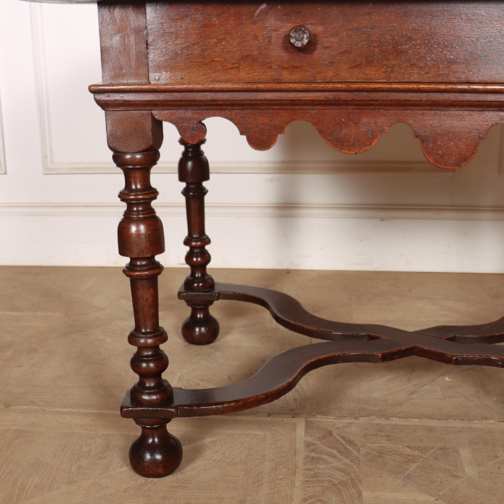 An 18th-century oak lamp table featuring a single drawer with brass knobs, a scalloped apron, turned legs, and an X-frame cross stretcher. View V