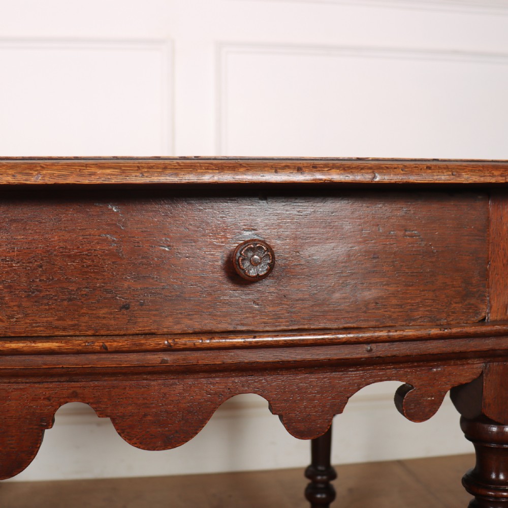 An 18th-century oak lamp table featuring a single drawer with brass knobs, a scalloped apron, turned legs, and an X-frame cross stretcher. View VI