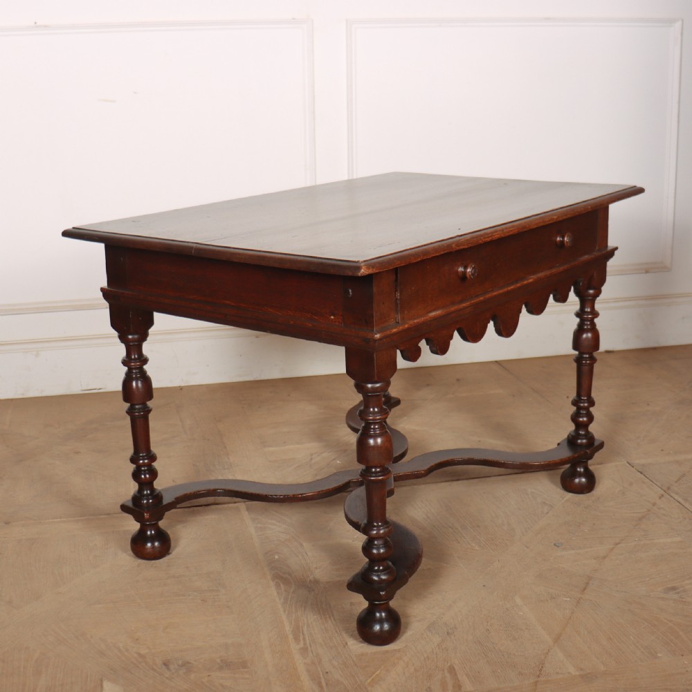 An 18th-century oak lamp table featuring a single drawer with brass knobs, a scalloped apron, turned legs, and an X-frame cross stretcher. View VII
