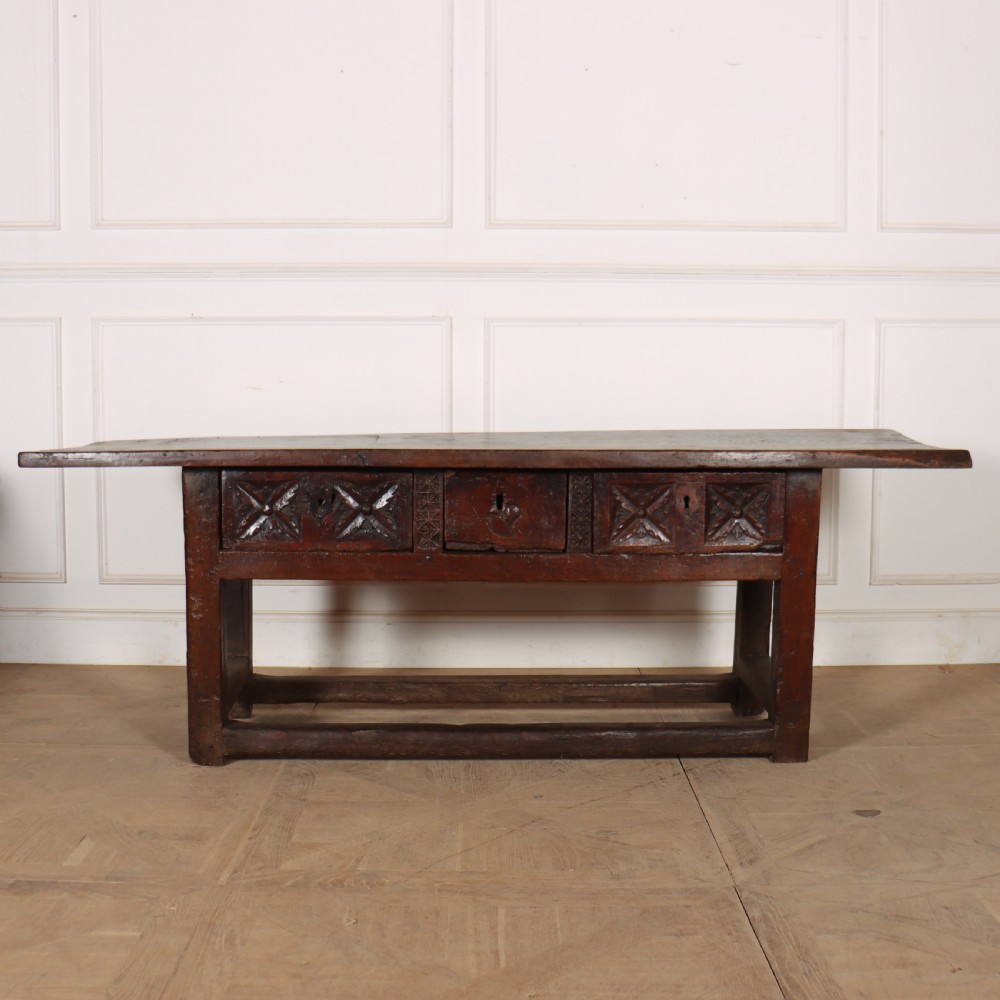 A 17th-century Spanish dark oak console table featuring a thick rectangular top over three geometric carved drawers, supported by sturdy legs with a perimeter stretcher.