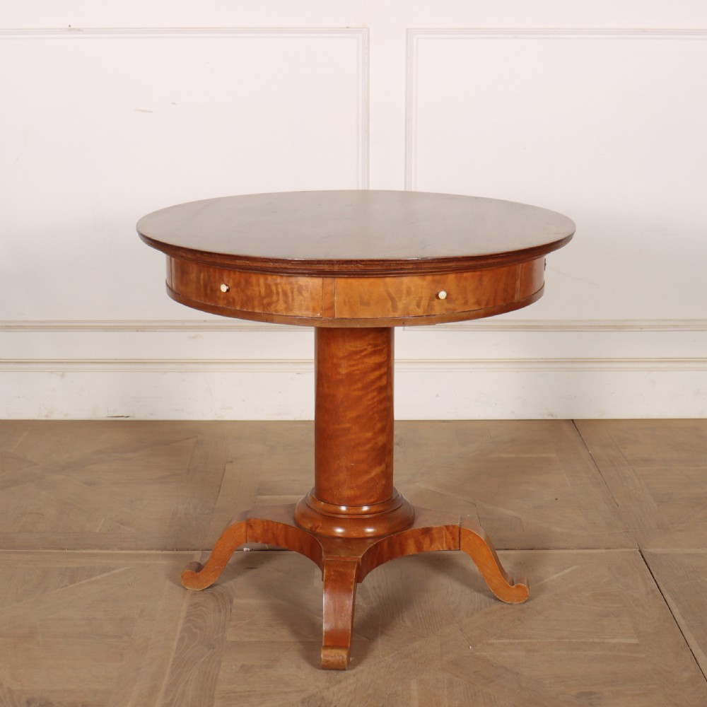 A 19th-century Swedish Biedermeier drum table in satin birch with a circular top, frieze drawers, central pedestal column, and four splayed legs.